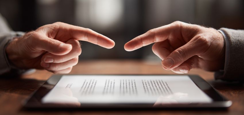 Close-up of two hands pointing at key clauses on a digital contract displayed on a tablet, highlighting the essential elements of contract law.