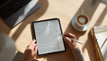 Business professional reviewing digital charts and analytics on a tablet at a sunlit workspace, with coffee and documents nearby, representing the analysis and preparation phase before finalizing a sales contract.